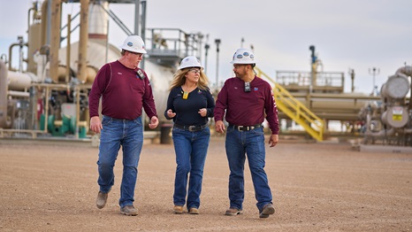 Collier central gathering facility, near Pecos, Texas. Workers walking in the facility with tanks and pipes in background.