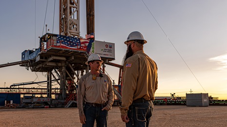 Two men talking to each other in front of an electric drilling rig at sunrise, in Carlsbad, New Mexico.