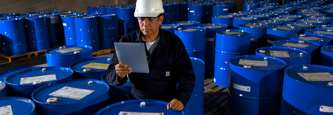Worker using a tablet with inventory software to take inventory of Chevron Meropa oil barrels at Sun Coast Resources in Houston, Texas.